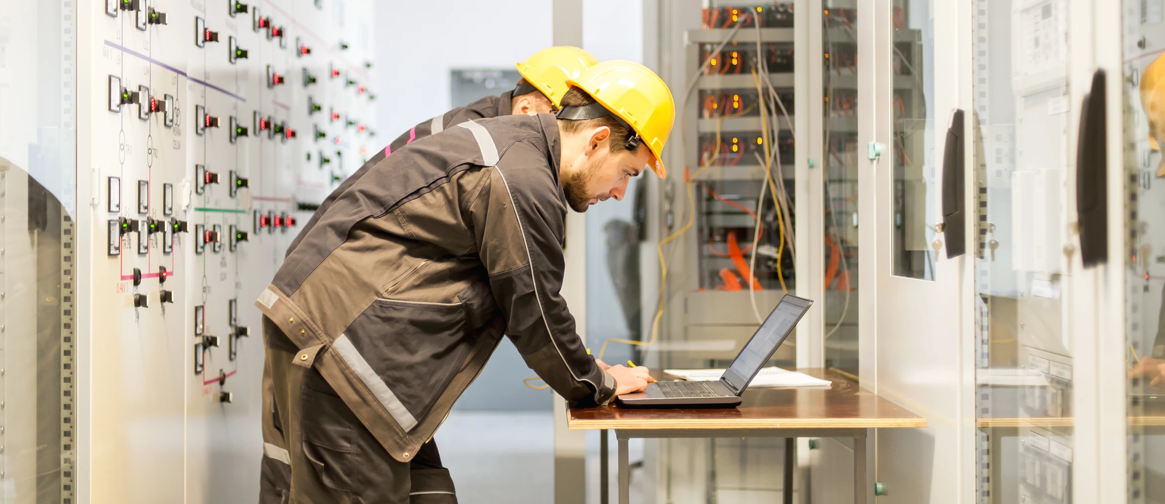 Ingénieur en tenue de sécurité avec casque jaune travaillant sur ordinateur portable dans salle de contrôle industrielle