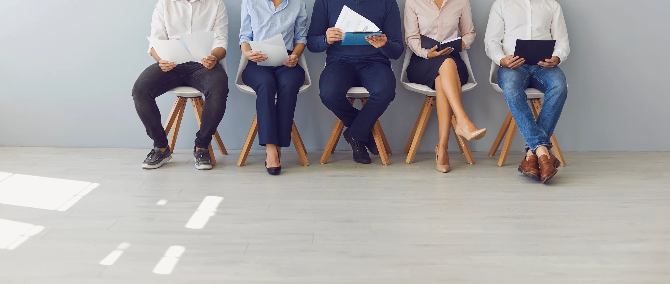 Quatre candidats en tenue professionnelle assis sur des chaises vertes dans une salle d'attente, tenant CV et documents, attendant un entretien d'embauche