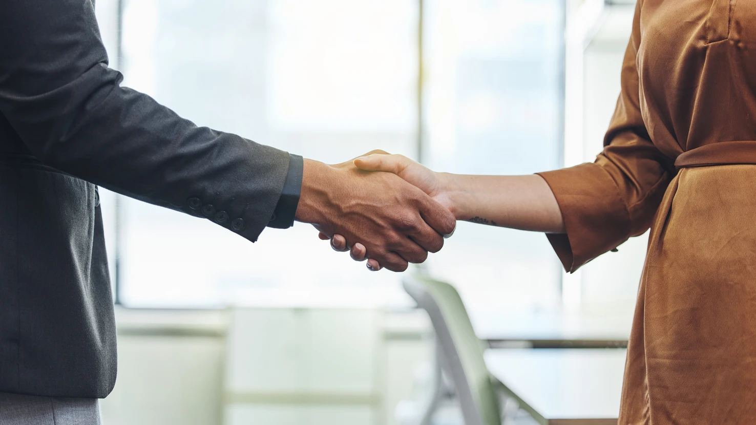 Deux personnes se serrent la main au-dessus d'un bureau blanc dans un environnement professionnel