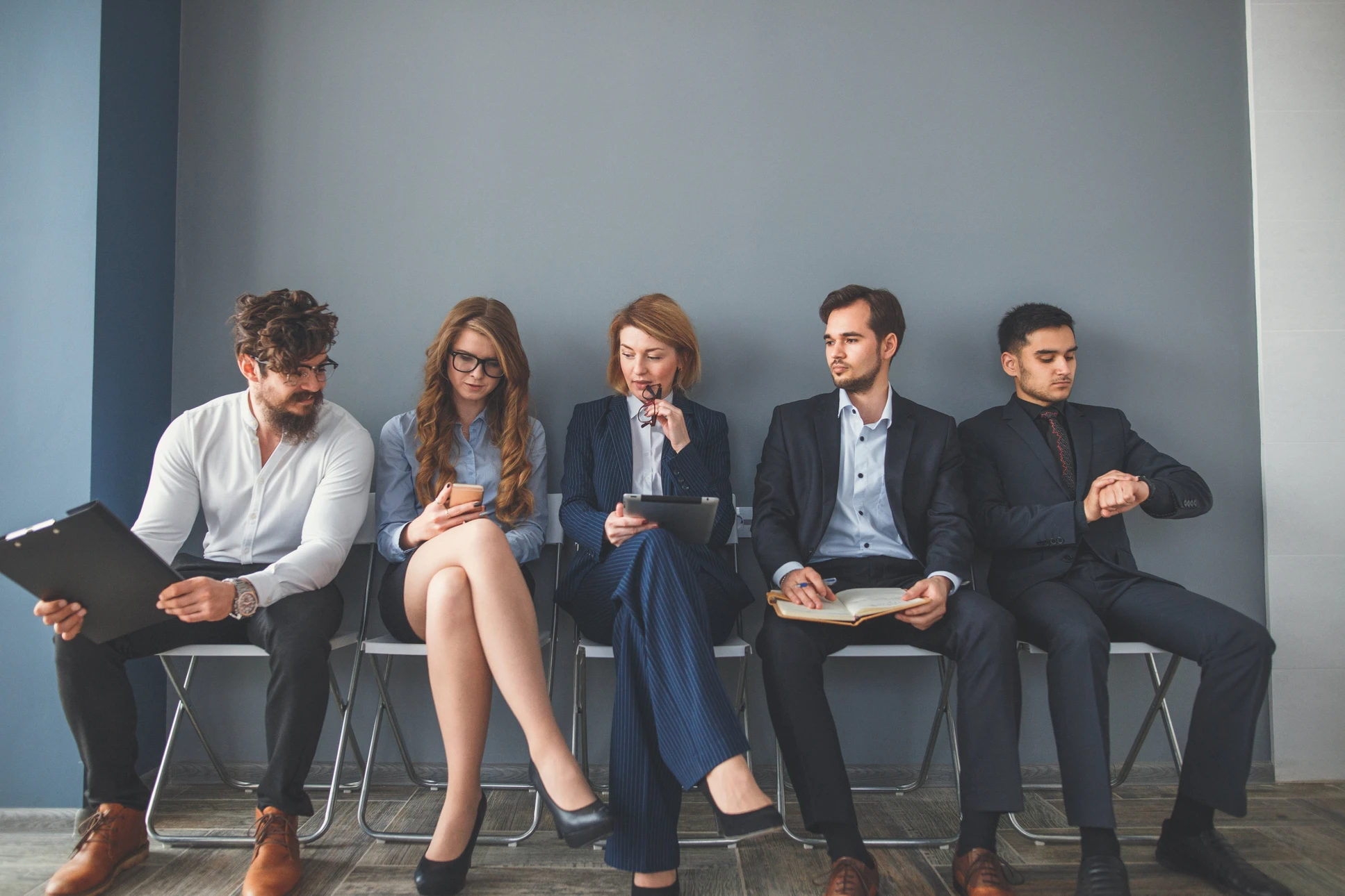 Quatre candidats en tenue professionnelle assis sur des chaises vertes dans une salle d'attente, tenant CV et documents, attendant un entretien d'embauche